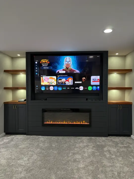 Built-in media wall with TV, electric fireplace, cabinets and lit floating shelves